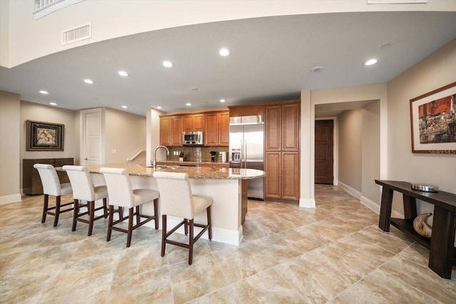 kitchen with a center island with sink, appliances with stainless steel finishes, decorative backsplash, a kitchen breakfast bar, and light stone countertops