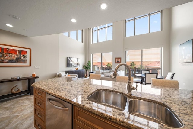 kitchen with light stone counters, sink, stainless steel dishwasher, and a towering ceiling