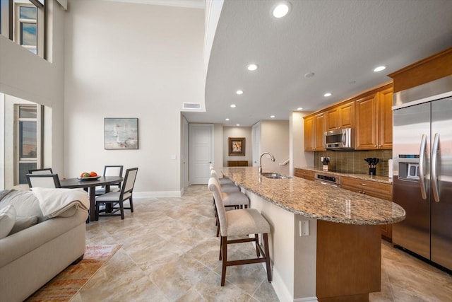 kitchen with stainless steel appliances, a kitchen bar, a center island with sink, and light stone countertops