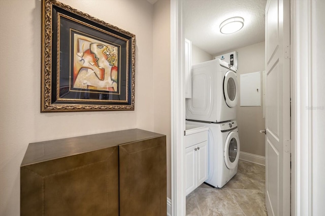 laundry room featuring a textured ceiling, cabinets, and stacked washer / dryer