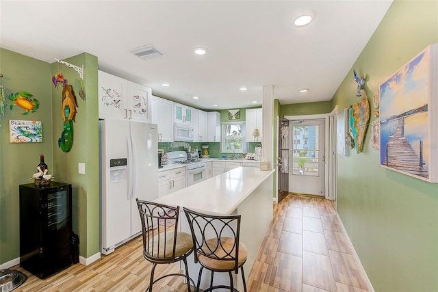 kitchen with white appliances, white cabinets, light wood-type flooring, a breakfast bar, and backsplash