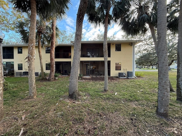 rear view of house with cooling unit, a balcony, and a yard