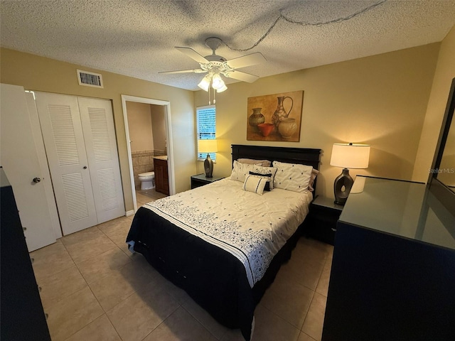 tiled bedroom featuring a textured ceiling, a closet, ensuite bath, and ceiling fan