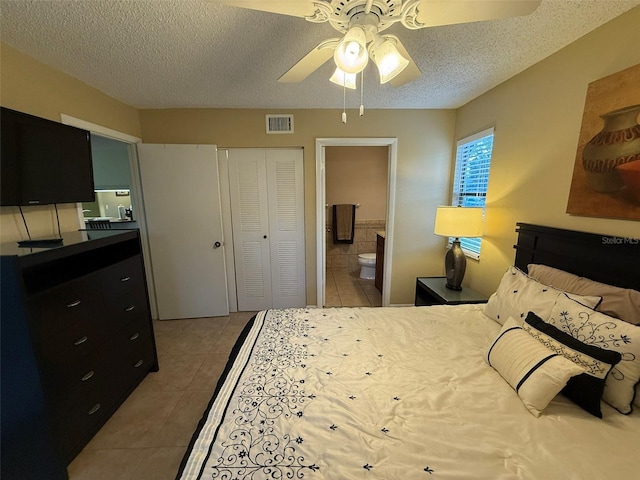 bedroom with a textured ceiling, ensuite bath, a closet, ceiling fan, and light tile patterned flooring