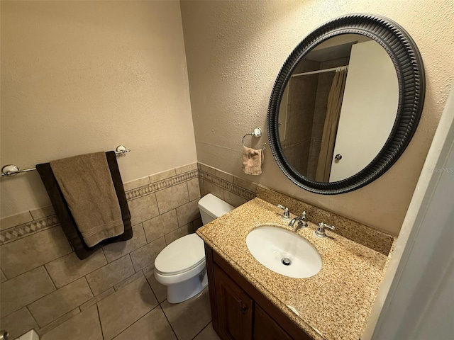 bathroom with toilet, walk in shower, tile walls, tile patterned flooring, and vanity