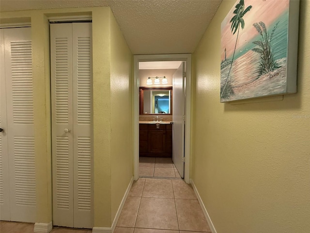 hall featuring sink, light tile patterned flooring, and a textured ceiling