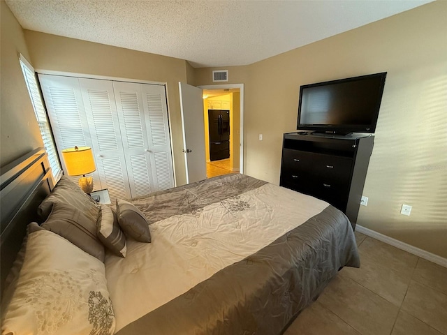 tiled bedroom featuring a closet, black refrigerator, and a textured ceiling