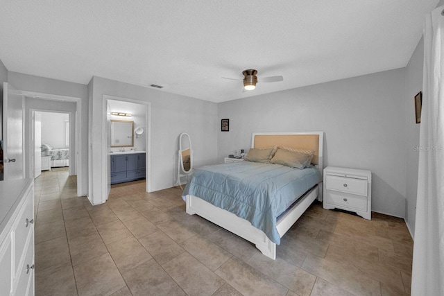 bedroom with light tile patterned flooring, ceiling fan, a textured ceiling, and ensuite bath