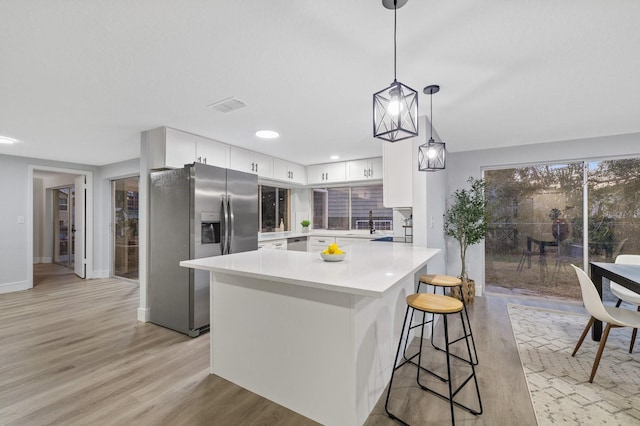 kitchen featuring white cabinetry, light hardwood / wood-style floors, stainless steel appliances, decorative light fixtures, and a breakfast bar