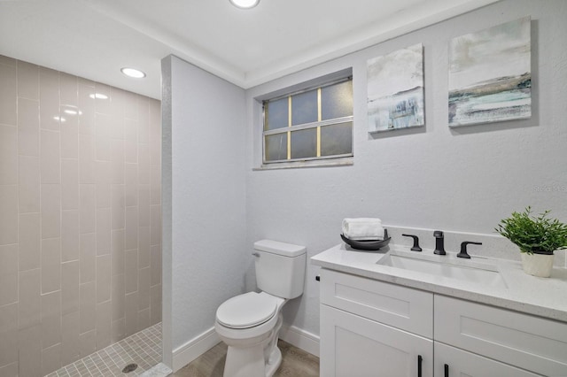 bathroom featuring wood-type flooring, tiled shower, vanity, and toilet