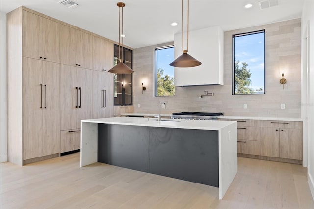 kitchen with tasteful backsplash, a wealth of natural light, hanging light fixtures, an island with sink, and light brown cabinetry