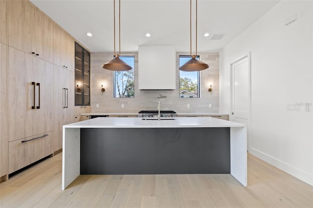 kitchen featuring decorative backsplash, sink, hanging light fixtures, and a center island with sink