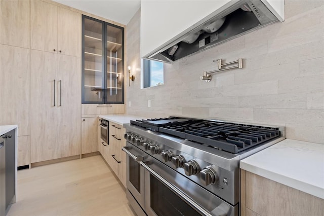 kitchen with appliances with stainless steel finishes, tasteful backsplash, light brown cabinetry, light hardwood / wood-style flooring, and custom range hood