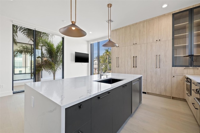 kitchen featuring decorative light fixtures, a kitchen island with sink, stainless steel dishwasher, light stone counters, and sink