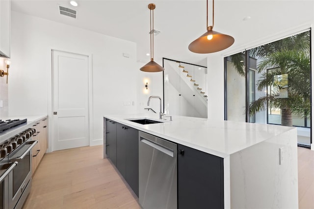 kitchen featuring an island with sink, stainless steel appliances, light wood-type flooring, pendant lighting, and sink