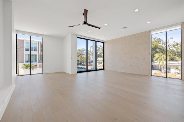 empty room featuring ceiling fan, expansive windows, and light wood-type flooring