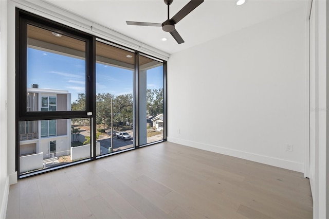 spare room featuring ceiling fan, expansive windows, and light wood-type flooring