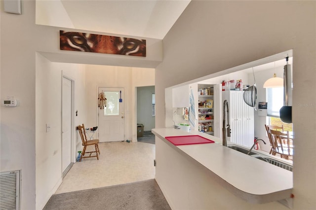 kitchen with lofted ceiling, light colored carpet, kitchen peninsula, and hanging light fixtures