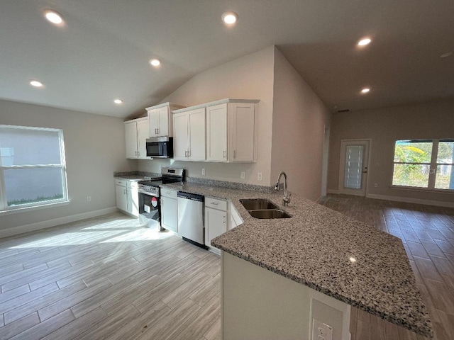 kitchen featuring vaulted ceiling, sink, light stone countertops, stainless steel appliances, and white cabinets