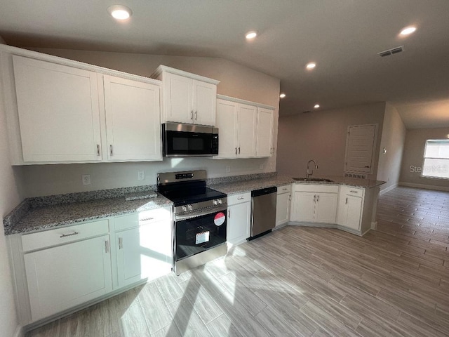 kitchen featuring white cabinetry, kitchen peninsula, appliances with stainless steel finishes, lofted ceiling, and sink