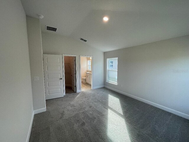 unfurnished bedroom with carpet, lofted ceiling, a walk in closet, connected bathroom, and a closet