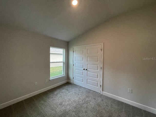 unfurnished bedroom featuring lofted ceiling, a closet, and carpet flooring