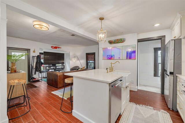 kitchen with pendant lighting, white cabinets, stainless steel appliances, a kitchen island with sink, and a breakfast bar area