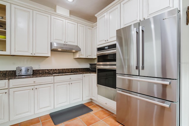 kitchen with white cabinetry, light tile patterned floors, dark stone counters, and appliances with stainless steel finishes