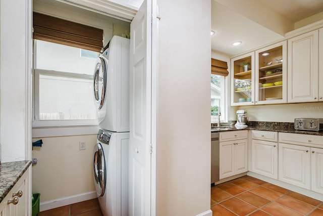 laundry area with light tile patterned flooring, stacked washer / dryer, and sink