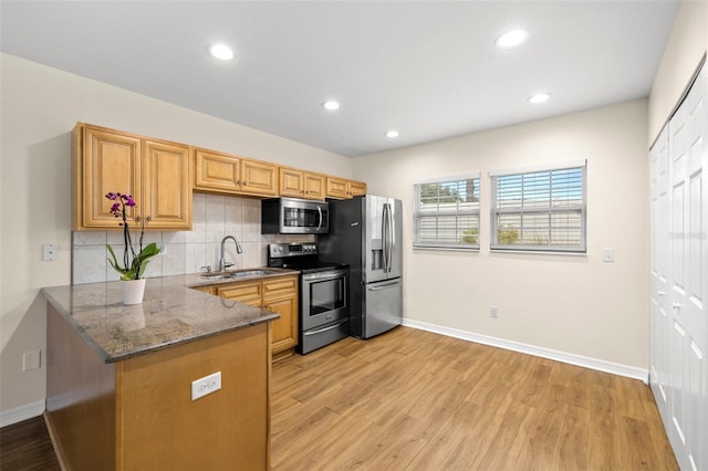 kitchen with sink, appliances with stainless steel finishes, tasteful backsplash, light hardwood / wood-style floors, and kitchen peninsula