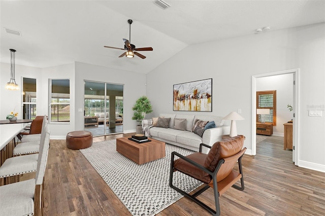 living room featuring ceiling fan with notable chandelier, dark wood-type flooring, and vaulted ceiling