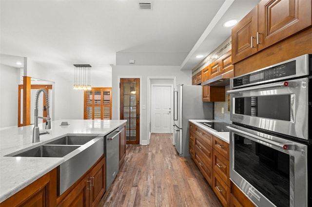 kitchen with sink, light stone counters, hanging light fixtures, hardwood / wood-style flooring, and stainless steel appliances