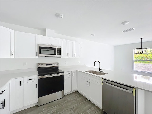 kitchen featuring a peninsula, a sink, white cabinetry, light countertops, and appliances with stainless steel finishes