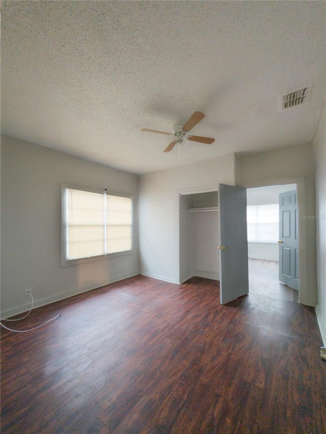 unfurnished room with ceiling fan, dark wood-type flooring, a wealth of natural light, and a textured ceiling