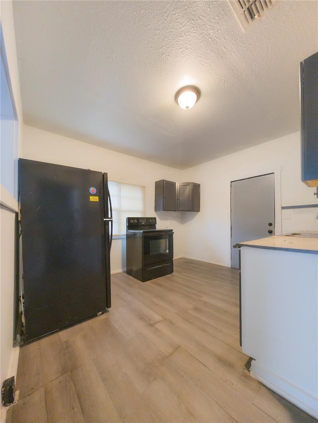 kitchen with light hardwood / wood-style floors, a textured ceiling, and black appliances