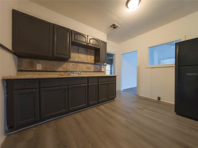 kitchen featuring hardwood / wood-style floors, black fridge, decorative backsplash, sink, and a textured ceiling