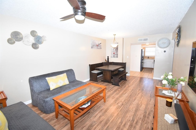 living room featuring a textured ceiling, ceiling fan, and light hardwood / wood-style floors