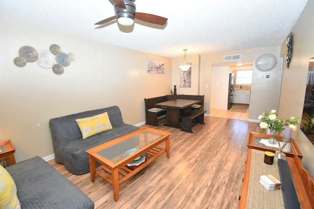 living room with a textured ceiling, ceiling fan, and light hardwood / wood-style floors