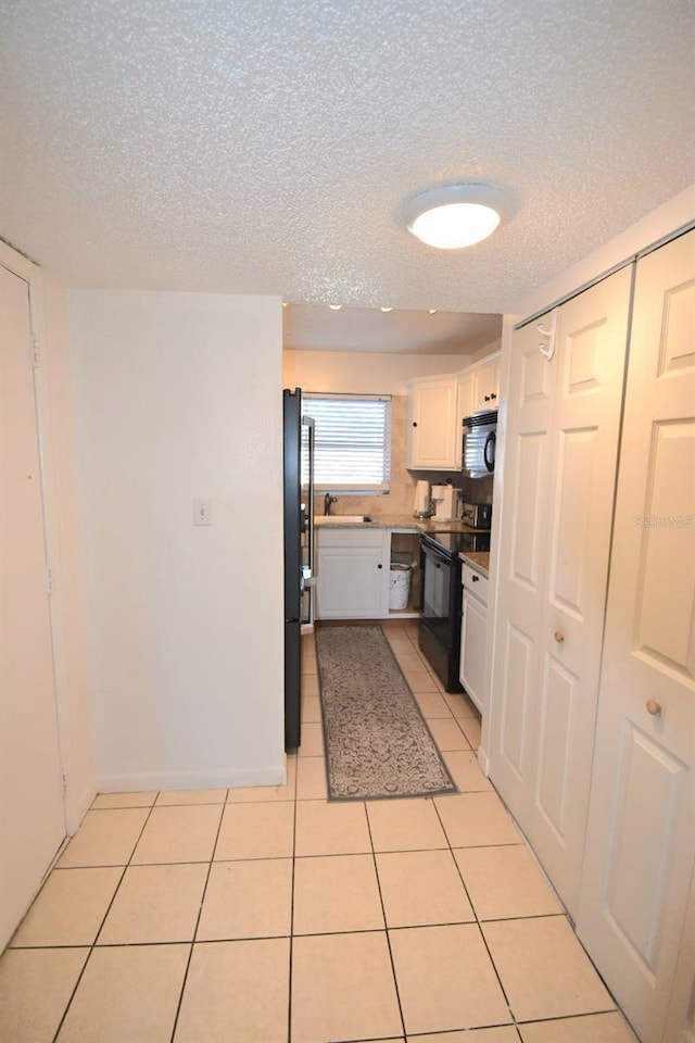 kitchen with a textured ceiling, white cabinets, black appliances, sink, and light tile patterned flooring