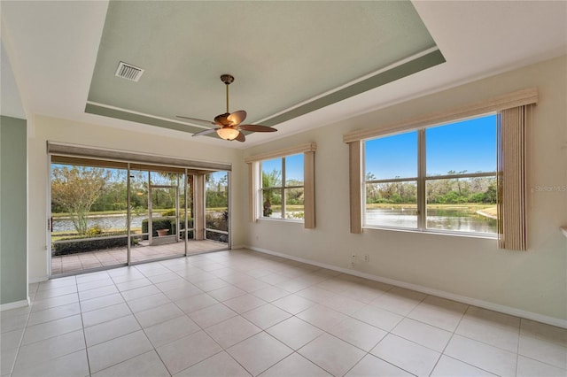 tiled empty room with a tray ceiling, ceiling fan, and a water view