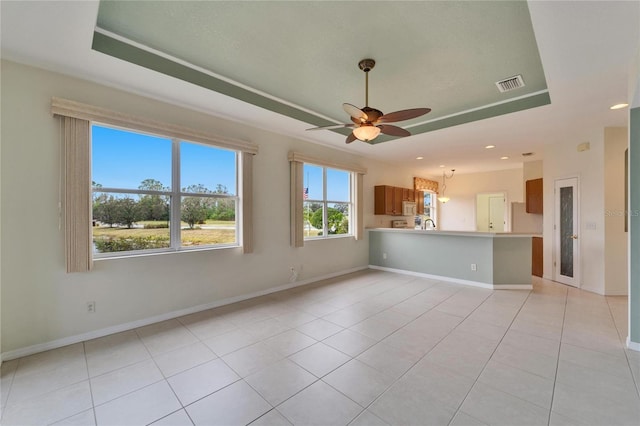 unfurnished living room with a raised ceiling, ceiling fan, and light tile patterned flooring