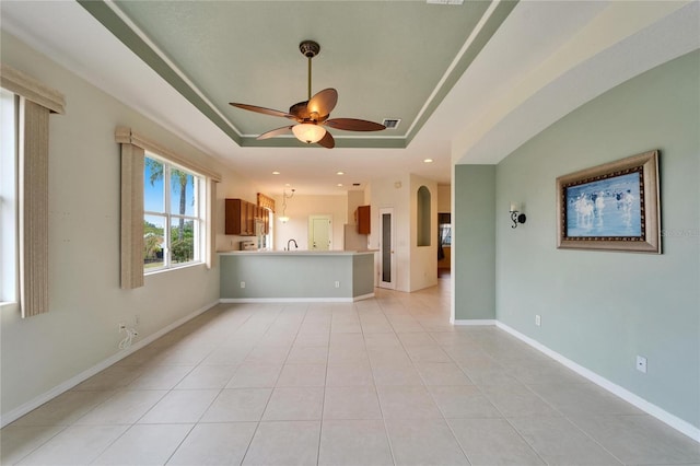 unfurnished living room with a raised ceiling, light tile patterned flooring, and ceiling fan