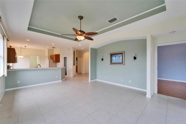 unfurnished living room featuring a raised ceiling, light tile patterned flooring, and ceiling fan