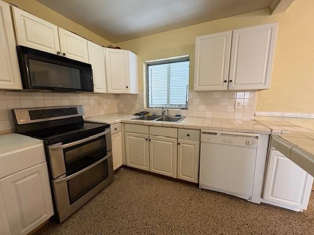 kitchen with white cabinets, dishwasher, tile counters, range with two ovens, and sink