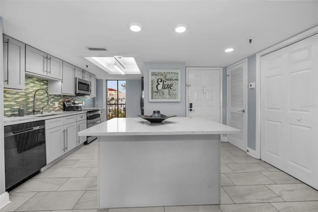 kitchen with a center island, stainless steel appliances, tasteful backsplash, sink, and gray cabinets