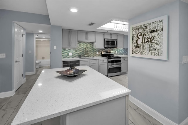 kitchen featuring appliances with stainless steel finishes, a kitchen island, tasteful backsplash, sink, and gray cabinets