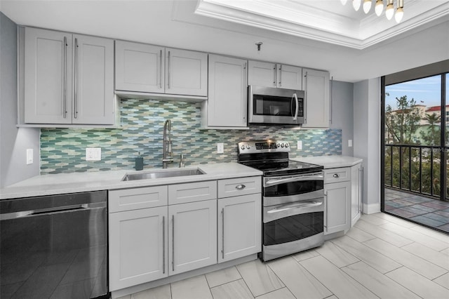 kitchen featuring stainless steel appliances, decorative backsplash, a raised ceiling, ornamental molding, and sink