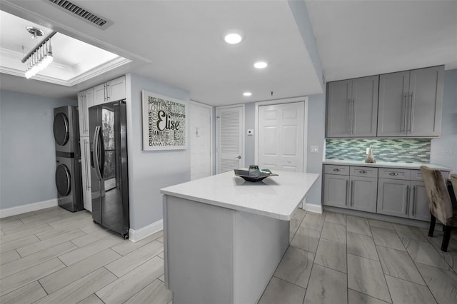 kitchen with tasteful backsplash, a kitchen island, stainless steel refrigerator with ice dispenser, stacked washer and dryer, and gray cabinetry