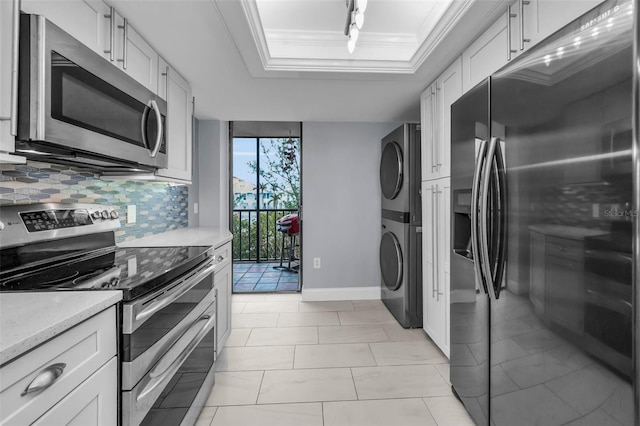 kitchen featuring stacked washer / dryer, appliances with stainless steel finishes, white cabinetry, a raised ceiling, and ornamental molding