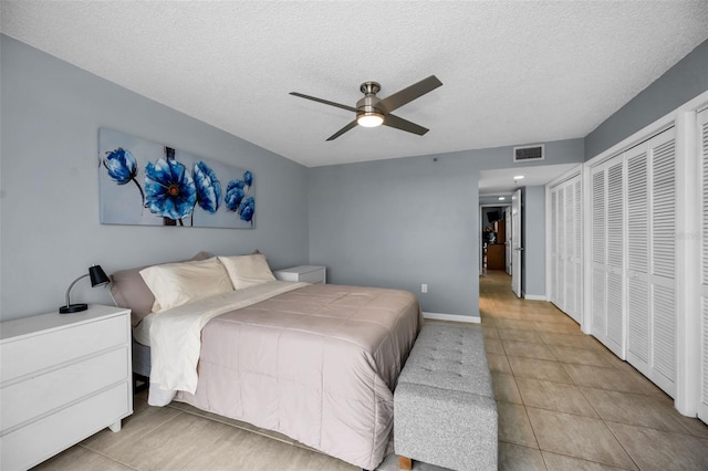 bedroom featuring ceiling fan, multiple closets, light tile patterned flooring, and a textured ceiling